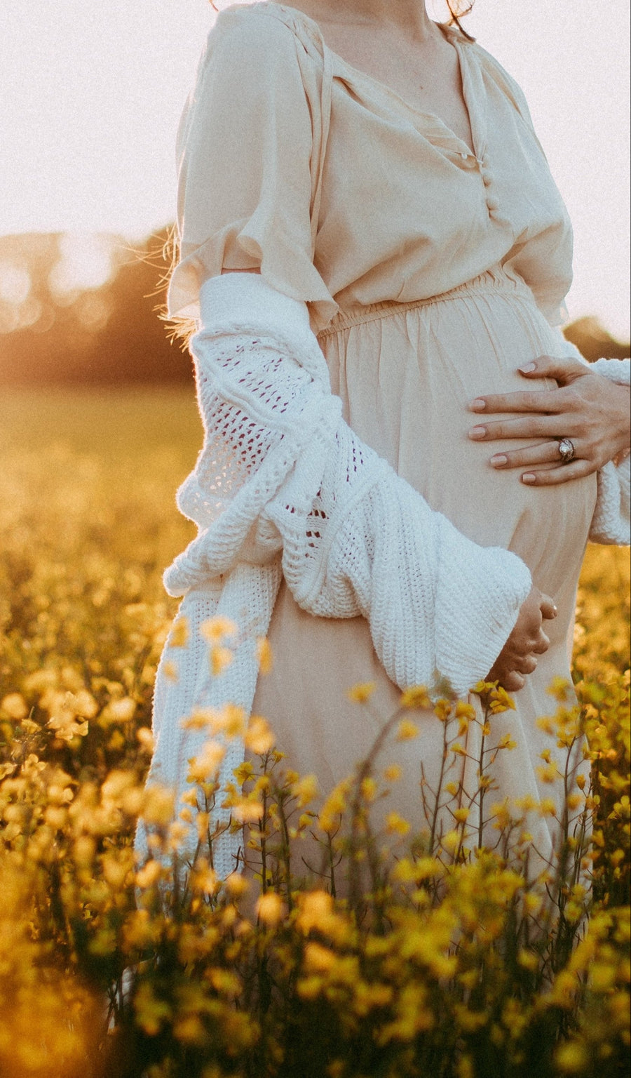 Lindsay in a sunlit field, holding her pregnant belly.